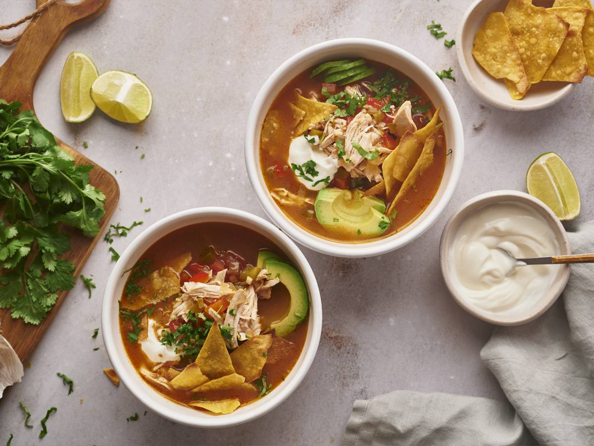 Slow Cooker Chicken Fajita Soup in tow bowls with shredded chicken, bell peppers, onions tortilla chips, and avocado.