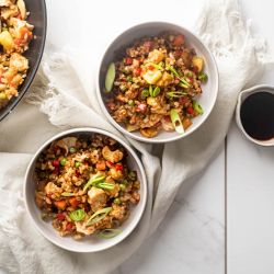 Chicken pineapple fried rice served in two bowls with fresh pineapple, chicken breast, brown rice, and vegetables with cashews.