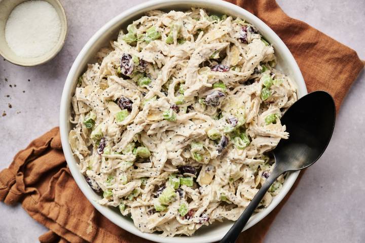 A bowl of cranberry almond chicken salad, garnished with a sprig of rosemary.