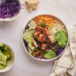 Asian salmon rice bowls with crispy salmon pieces served with rice, purple cabbage, edamame, carrots, and cucumber.