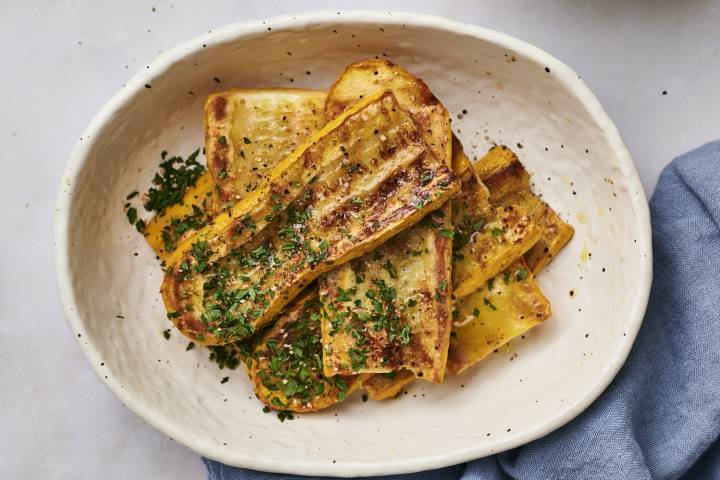Grilled yellow squash on a black plate sprinkled with parsley.