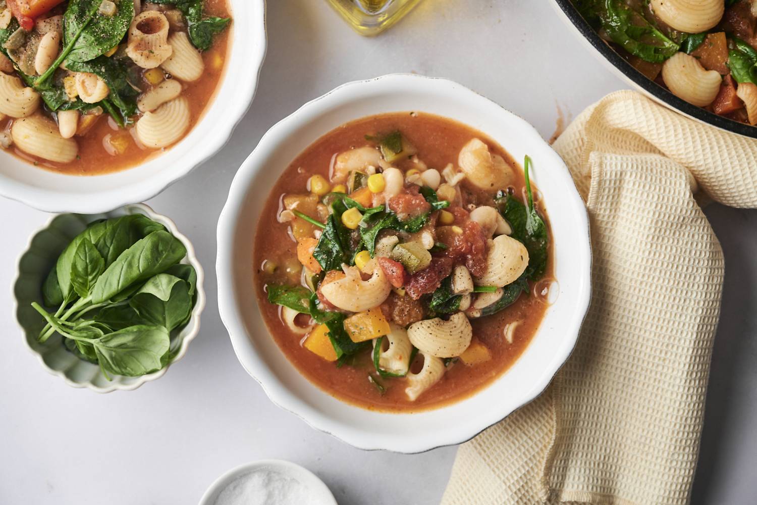 A cozy bowl of garden minestrone packed with shell pasta, corn, spinach, white beans, and vibrant vegetables in a savory tomato broth.