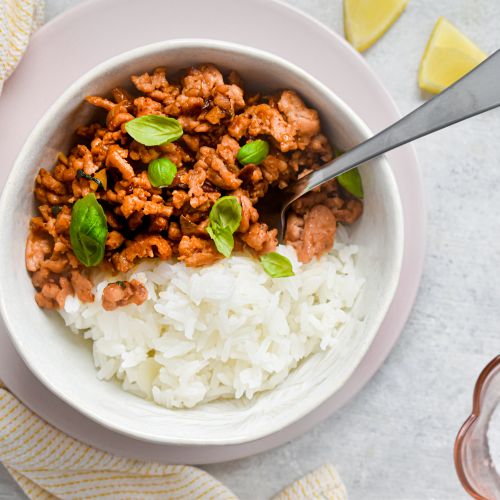 Thai basil ground turkey in a bowl with white rice and Thai basil leaves. 