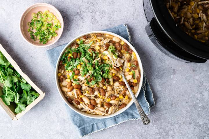 A hearty bowl of chicken chili topped with fresh cilantro and sliced green onions. A dish of green onions and fresh cilantro beside it, exuding a cozy feel.